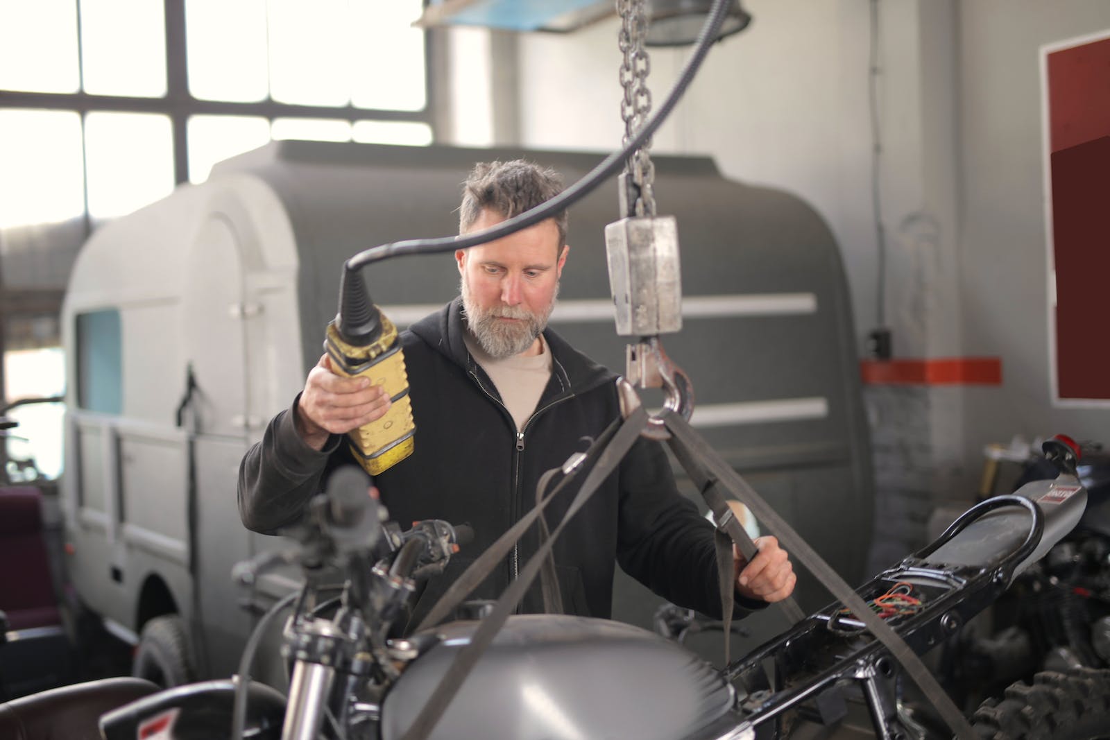 Male mechanic using hydraulic crane in garage